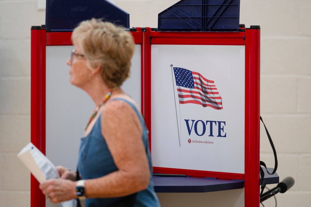 A woman walks past a voting booth with an American flag and the word “VOTE” displayed on the side.