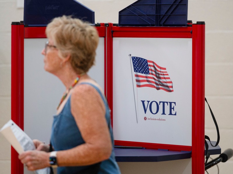 A woman walks past a voting booth with an American flag and the word “VOTE” displayed on the side.