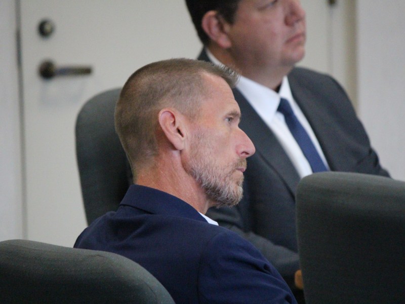 Man in navy jacket tilts his head as he listens to court proceedings.