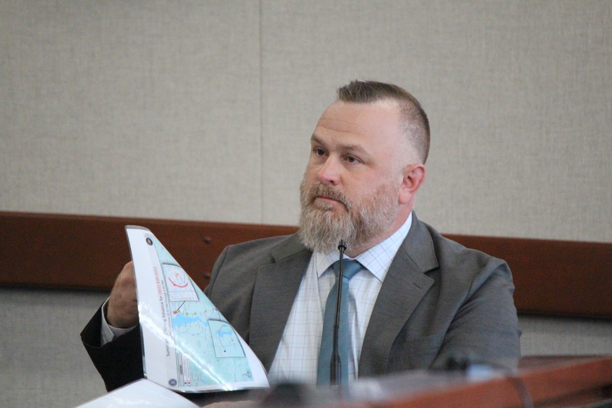 Man with tie and jacket on holds laminated page as he testifies in court.