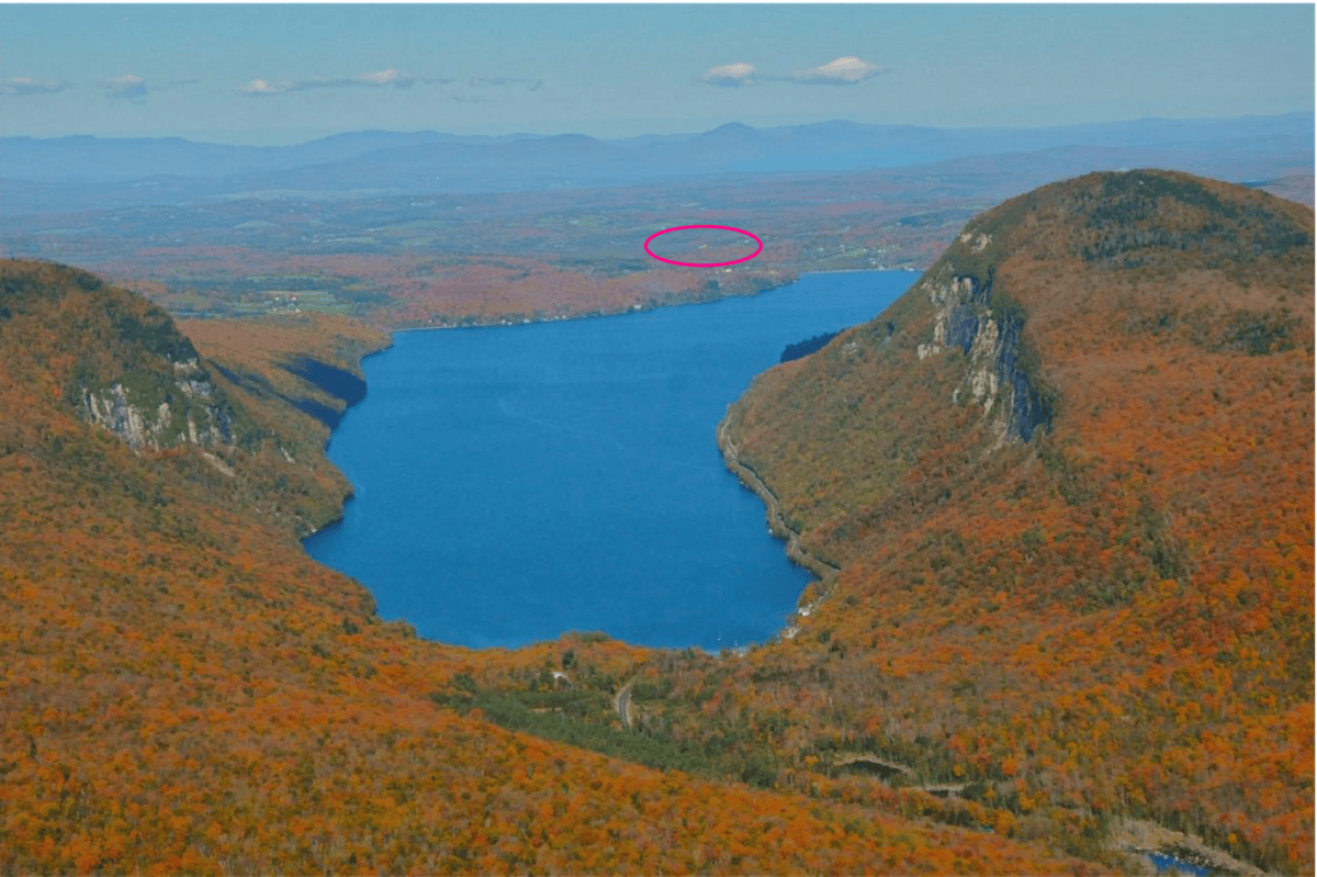 A large blue lake sits between two forested hills under a clear sky, with an area circled in pink in the distant landscape.