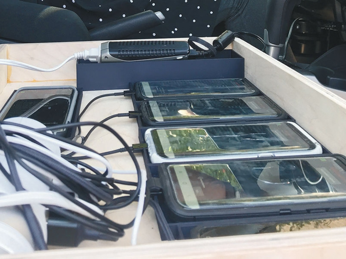 Four smartphones connected to a power strip charging inside a wooden drawer.