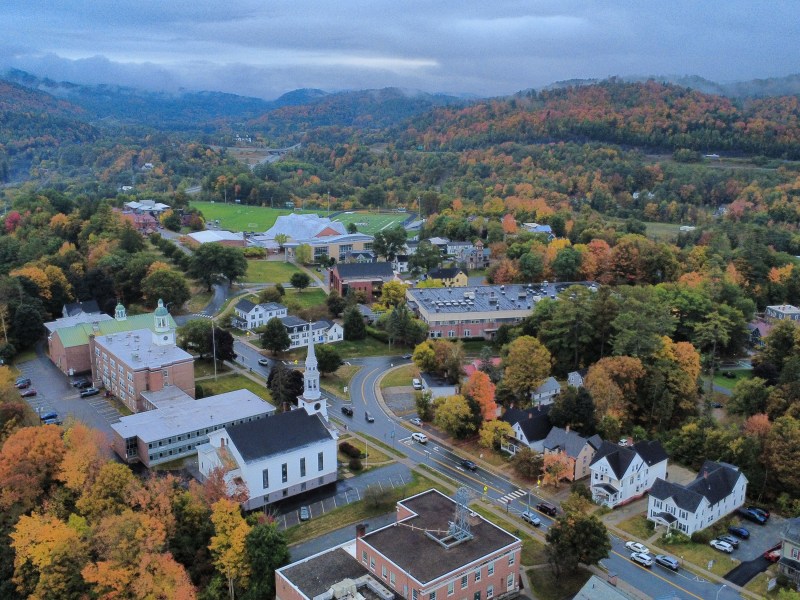 Aerial view of a campus nestled among forested hills in peak autumn foliage.