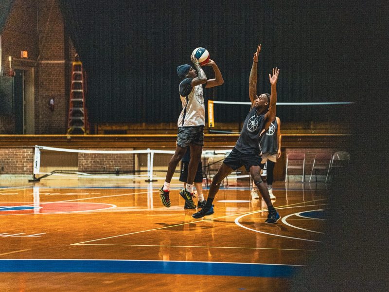 A basketball player jumps to shoot the ball while being defended by another player on an indoor court.