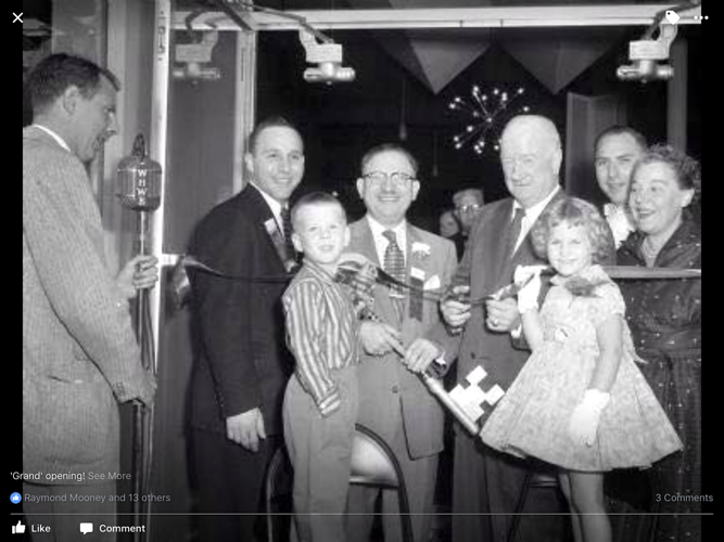 A group of people, including two children, cutting a ribbon with a large ceremonial key at a grand opening ceremony.