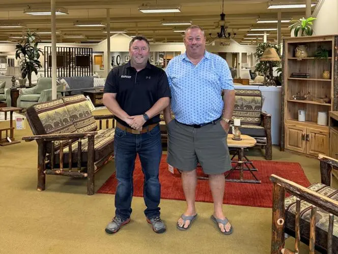 Two men standing in a furniture showroom filled with log-style wooden furniture.